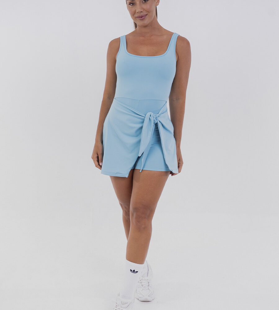 Vestido macaquinho azul Azzure com short interno e saia sobreposta, amarração lateral ajustável e tecido com toque gelado e proteção UV 50+. Ideal para esportes como beach tennis e momentos de lazer.